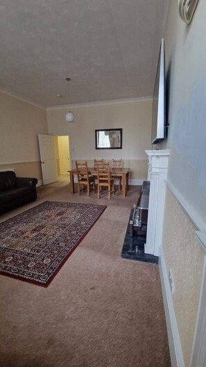 A living room with a dark-colored sofa, a patterned rug, a dining table with chairs, and a fireplace. - Spacious Clean Central Near Train Stn & University (Edinburgh)