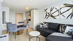 Ein modernes Wohnzimmer mit einer schwarzen Couch, grauen Sesseln, einem kleinen runden Tisch und abstrakter Kunst an der Wand.