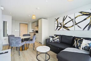 Ein modernes Wohnzimmer mit einer schwarzen Couch, grauen Sesseln, einem kleinen runden Tisch und abstrakter Kunst an der Wand.