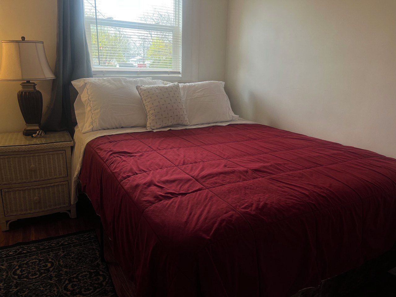 Een slaapkamer met een bed, een nachtkastje, een lamp en een raam met gordijnen.
