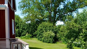Un patio in legno con una panchina e un tavolo, un edificio rosso con decorazioni bianche e un prato curato con alberi.