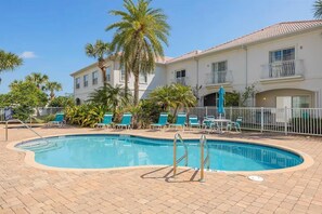 A swimming pool with lounge chairs and a fenced area, surrounded by palm trees and a building with balconies. - Walk to the beach. Two pools, hot tub, tennis. (St. Augustine)