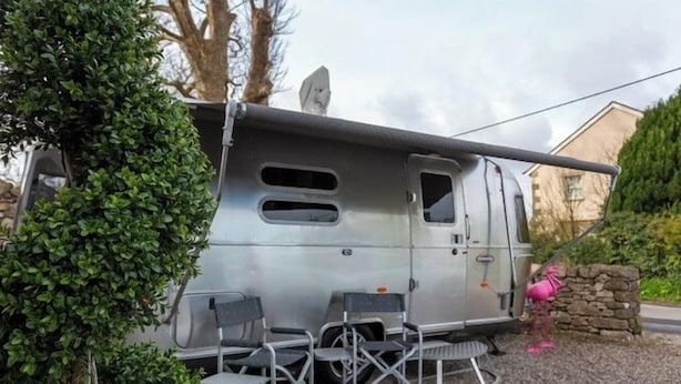 A stationary RV with a covered area, a satellite dish, and a small table with chairs. - Unique Airstream Retreat - Sleeps 2 - Free Parking (Carnforth)