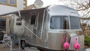 A silver recreational vehicle with a covered living area, a small step leading to the entrance, and two pink flamingo decorations. - Unique Airstream Retreat - Sleeps 2 - Free Parking (Carnforth)