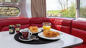 A dining table with croissants, a cup of coffee, and a glass of orange juice in a red upholstered booth. - Unique Airstream Retreat - Sleeps 2 - Free Parking (Carnforth)