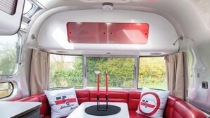 A bus interior with a red leather couch, a small table, and a window with a view of greenery. - Unique Airstream Retreat - Sleeps 2 - Free Parking (Carnforth)