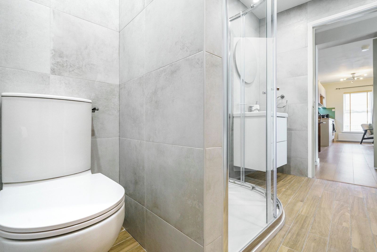 A modern bathroom with a toilet, shower enclosure, and a glimpse of a kitchen area.