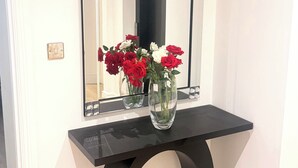 A black console table with a mirror above it, reflecting a doorway and a vase with red and white flowers. - Private Elevator Marylebone Apartment Central Lond (London)