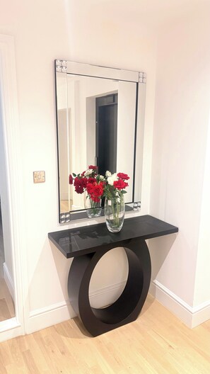 A black console table with a mirror above it, reflecting a doorway and a vase with red and white flowers. - Private Elevator Marylebone Apartment Central Lond (London)