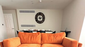 A modern living room with a sofa, a dining table, and a wall clock. - Private Elevator Marylebone Apartment Central Lond (London)