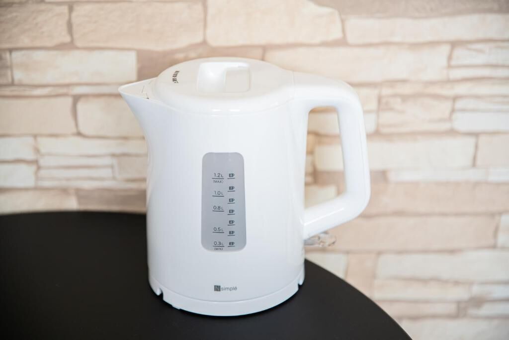 A white electric kettle with a digital display and a handle, placed on a black surface against a stone wall background.