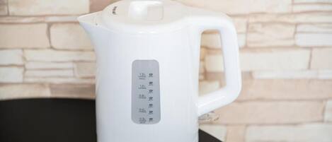 A white electric kettle with a digital display and a handle, placed on a black surface against a stone wall background.