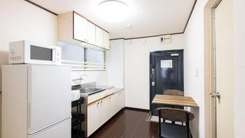 A compact kitchen with a microwave, refrigerator, and a small dining table with a chair.
