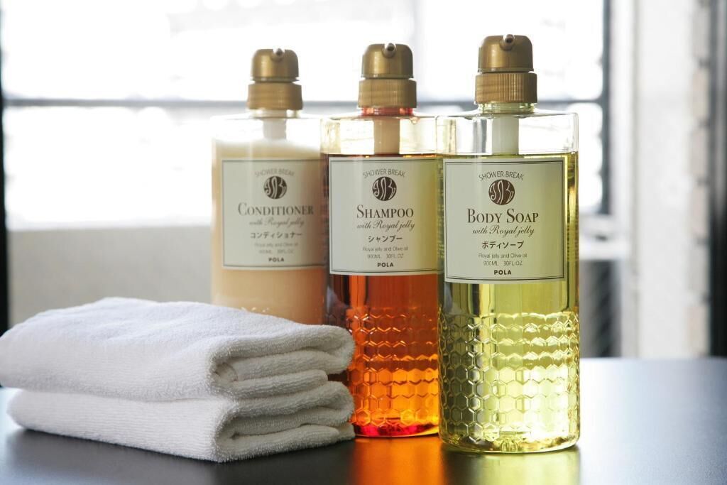 Three bottles of shower products on a table with a folded towel.