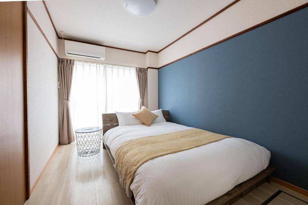Une chambre à coucher avec un lit, une fenêtre avec des rideaux, un appareil de climatisation et une petite table ronde.