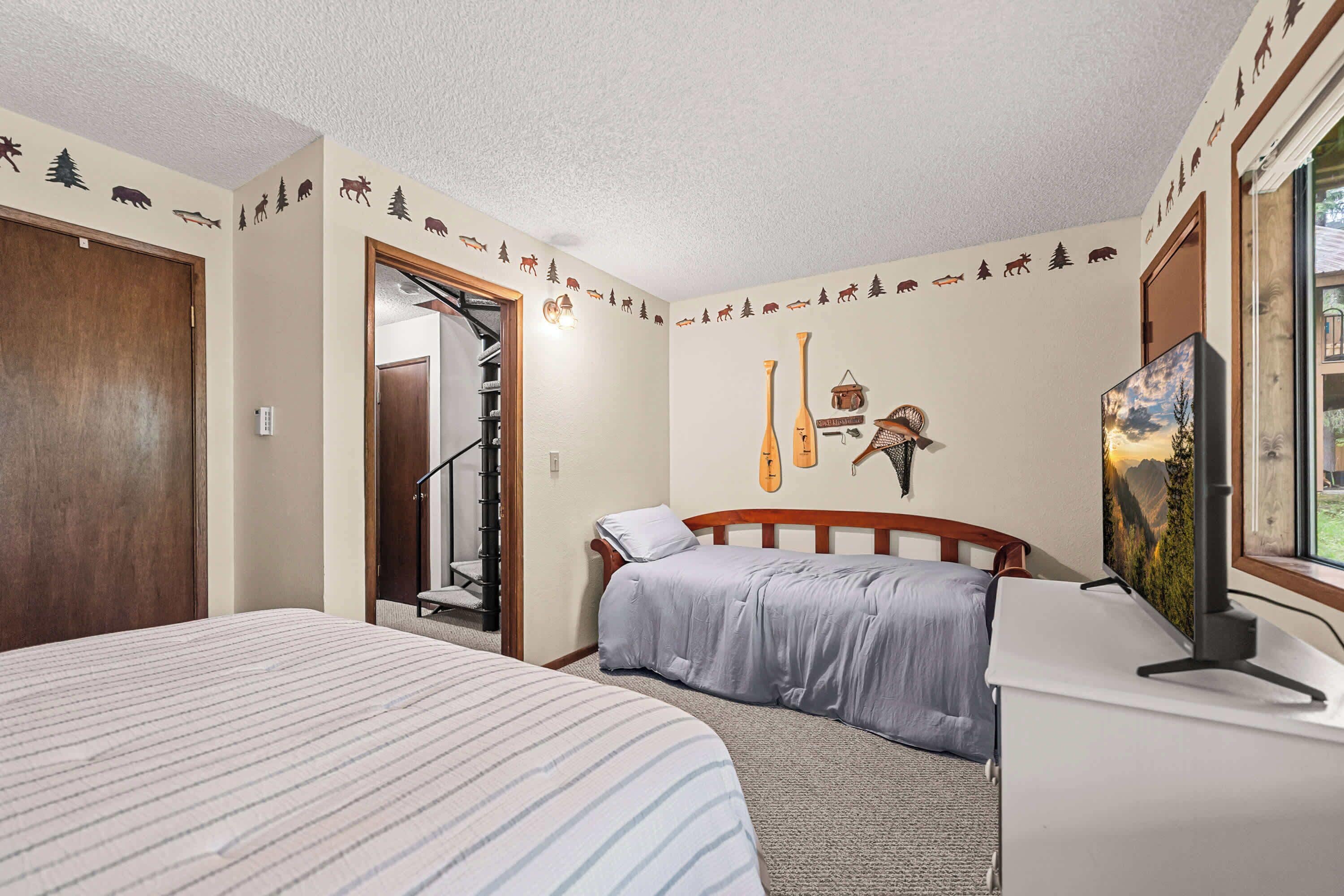A bedroom with a bed, a desk, a chair, a painting, and a wall with animal and tree decals.