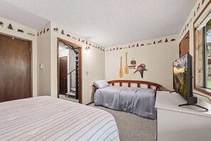 Un dormitorio con cama, escritorio, silla, un cuadro y una pared decorada con motivos de animales y árboles.