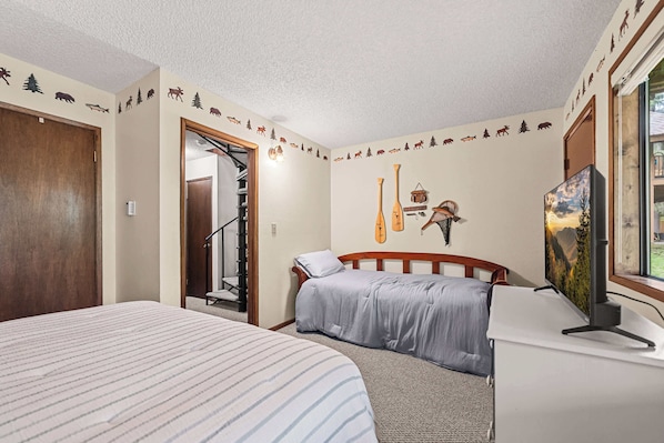 A bedroom with a bed, a desk, a chair, a painting, and a wall with animal and tree decals. - Limber Pine Townhome and 2BDR Stay (Whitefish)