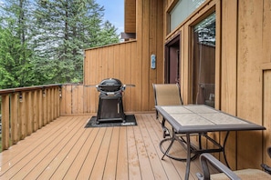 A wooden deck with a grill, a table, and a chair. - Limber Pine Townhome and 2BDR Stay (Whitefish)