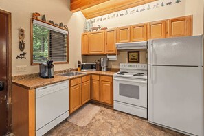 A kitchen with wooden cabinets, a white dishwasher, a stove, and a refrigerator. - Limber Pine Townhome and 2BDR Stay (Whitefish)