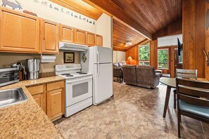 A kitchen with wooden cabinets, a stove, a refrigerator, and a dining area with a table and chairs. - Limber Pine Townhome and 2BDR Stay (Whitefish)