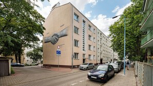Um edifício com um grande mural de duas mãos estendidas, uma placa de proibição de estacionamento e carros estacionados ao longo da rua.