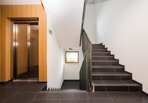A modern interior with a wooden elevator, a staircase, and a small window. - Wola Jaktorowska Urban Studio (Warszawa)