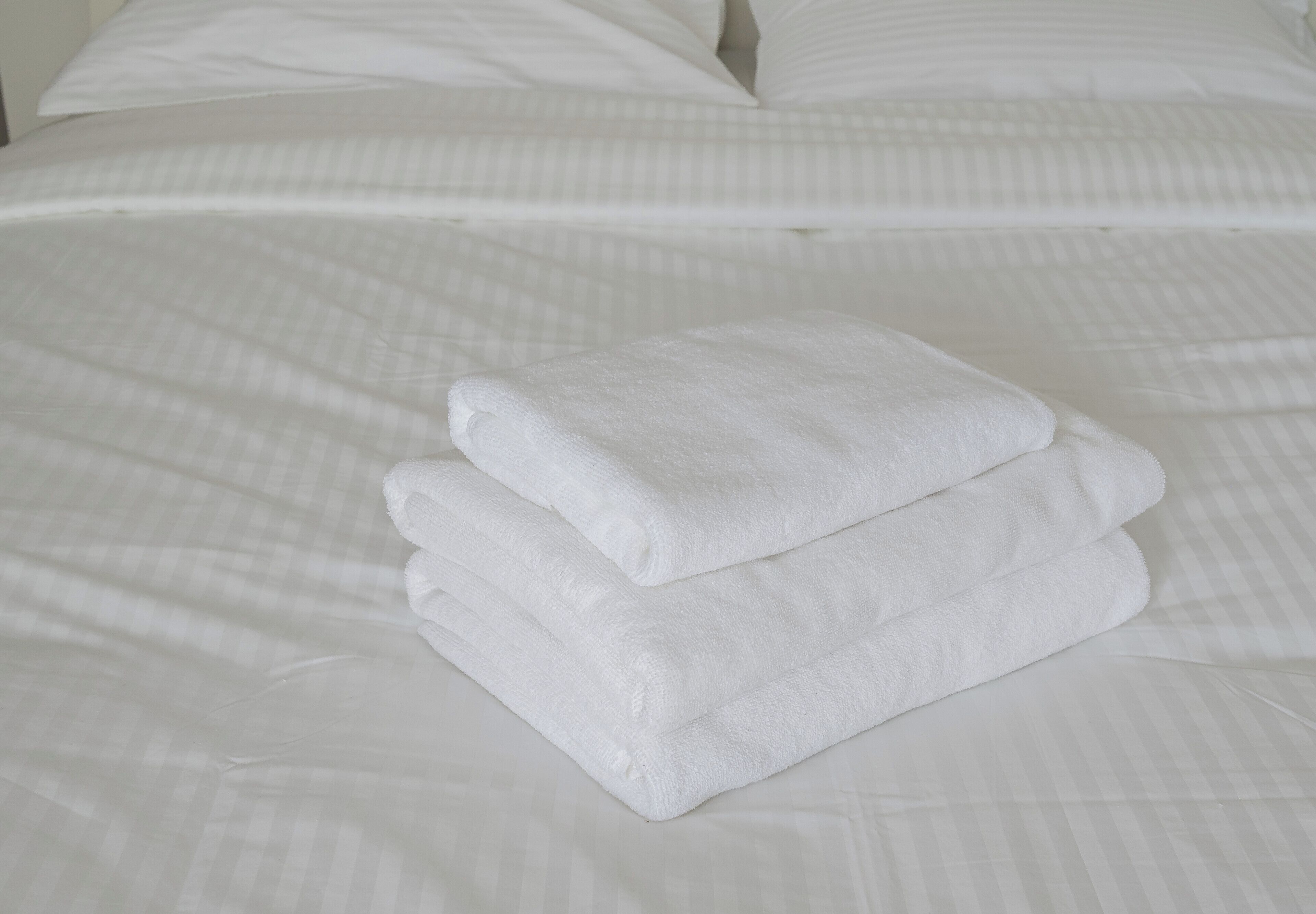 A neatly made bed with white linens and a folded white towel on top.