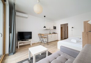 Un espacio habitable moderno y minimalista con televisión de pantalla plana, comedor, kitchenette y cama.