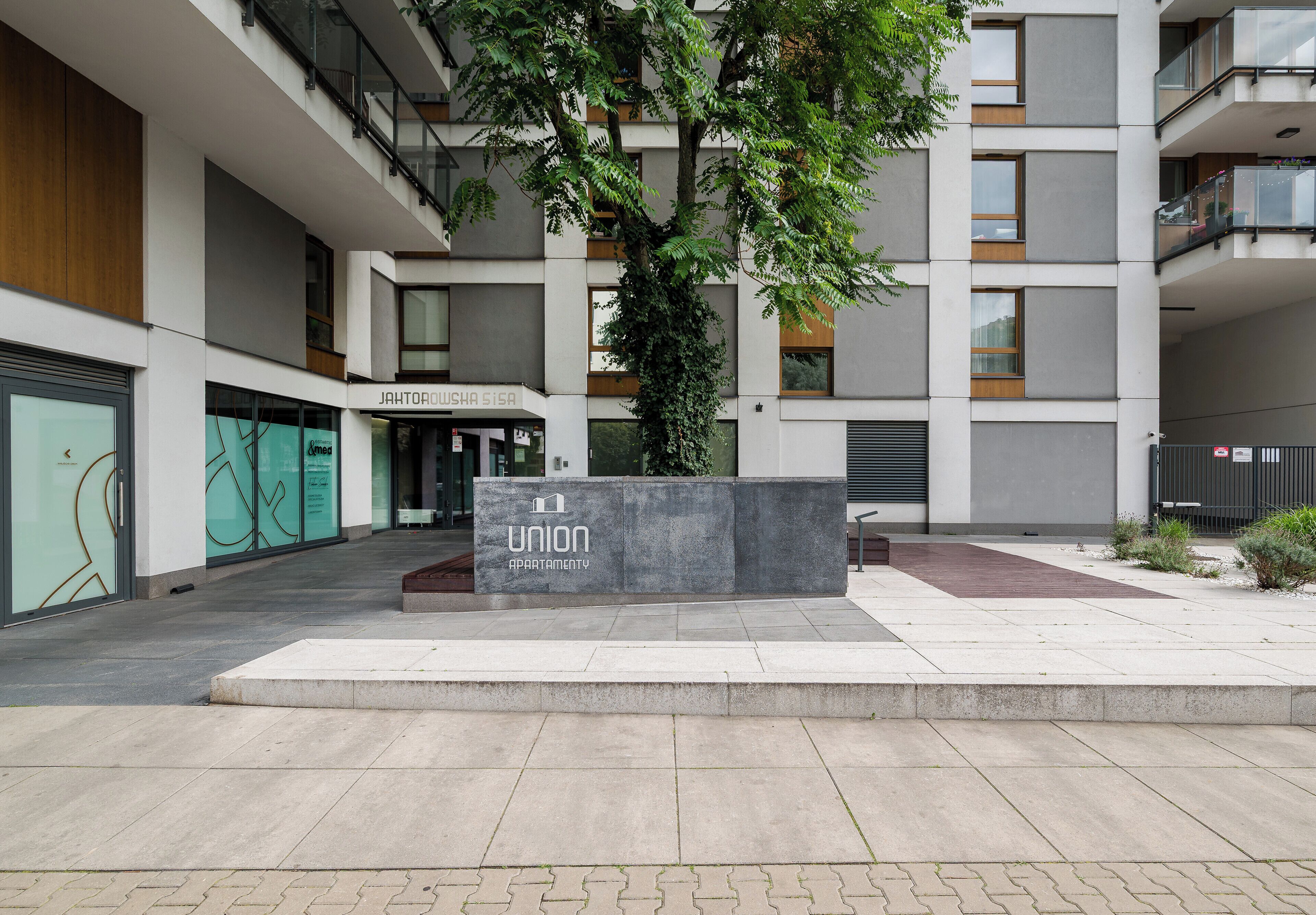 Un immeuble d’appartements moderne, avec une enseigne indiquant « Union Apartment » et un arbre au centre.