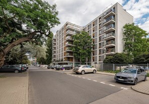 Ein mehrstöckiges Wohngebäude mit Balkonen, parkenden Autos und Bäumen.