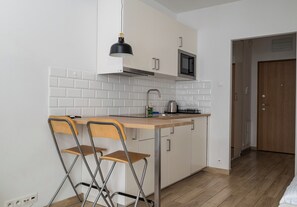 A compact kitchen with white tiled backsplash, a microwave, a sink, and two foldable chairs. - Wola Jaktorowska Urban Studio (Warszawa)