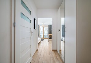 A hallway with a wooden floor leading to a room with a bed and a table. - Wola Jaktorowska Urban Studio (Warszawa)