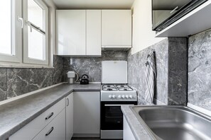 A compact kitchen with white cabinets, a built-in oven, a gas stove, and a stainless steel sink. - Baltic Seaside Homely Apartment (Gdańsk)
