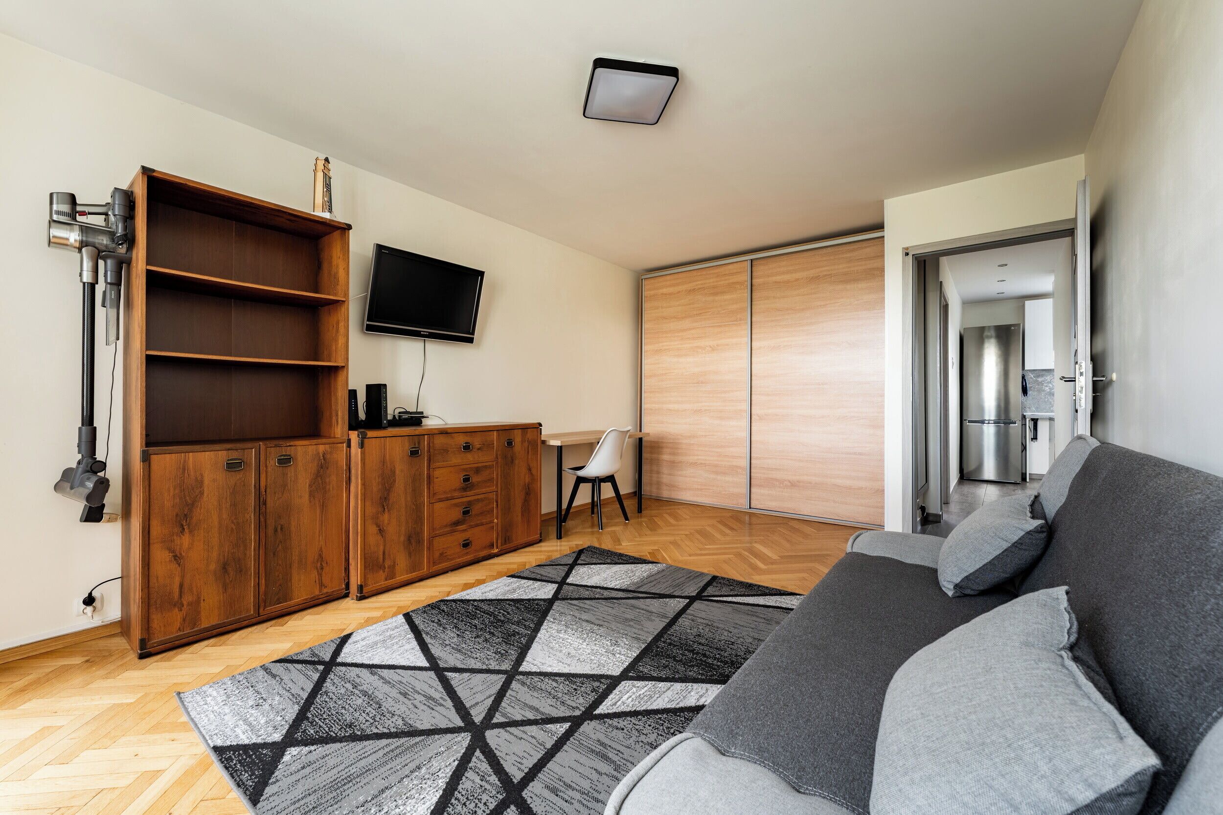 Un salon moderne avec un canapé, un meuble en bois, un téléviseur à écran plat et un tapis à motifs.