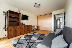 A modern living room with a sofa, a wooden cabinet, a flat-screen TV, and a patterned rug. - Baltic Seaside Homely Apartment (Gdańsk)