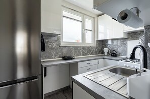 A modern kitchen with a stainless steel refrigerator, a gas stove, and a window. - Baltic Seaside Homely Apartment (Gdańsk)
