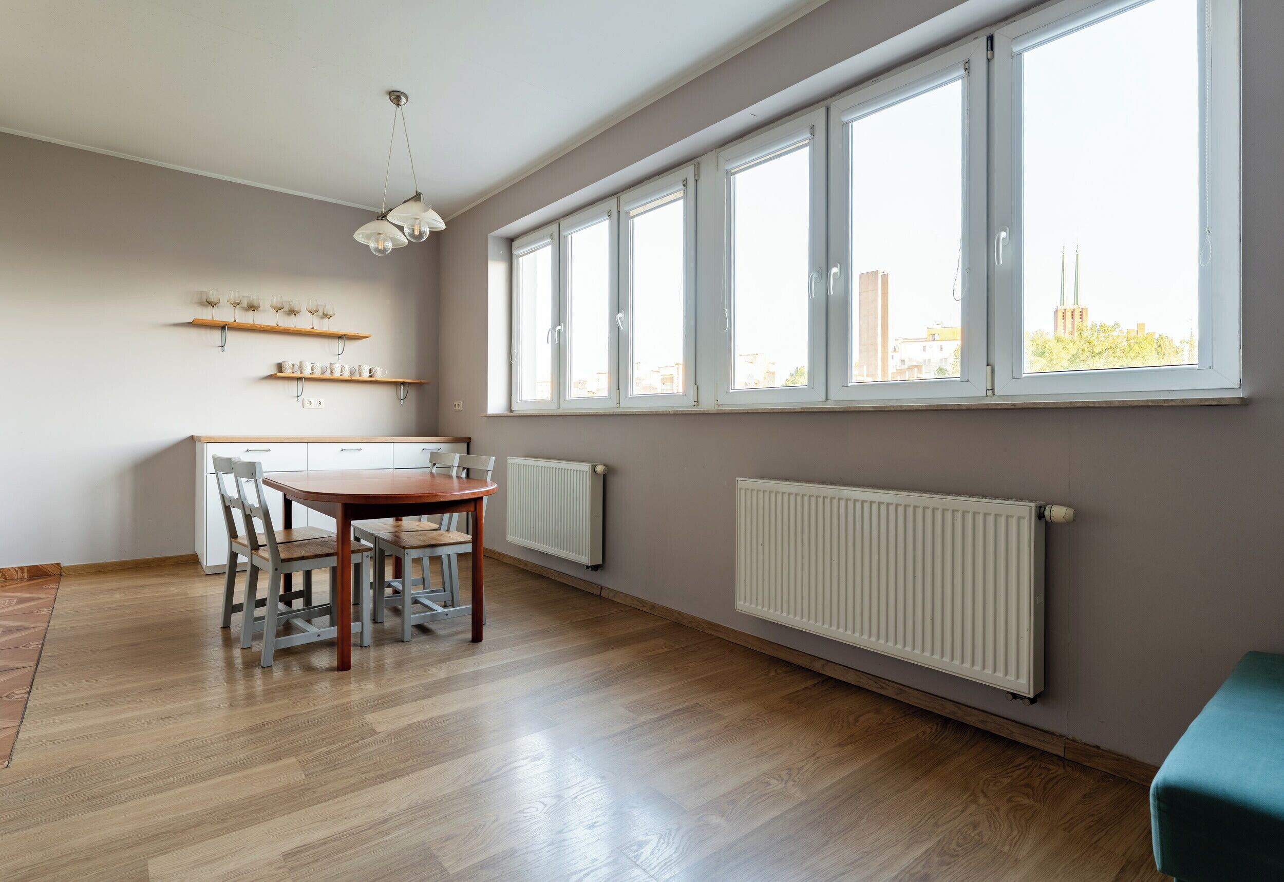 Un coin repas avec une table et des chaises en bois, un luminaire suspendu et une fenêtre donnant sur des immeubles.