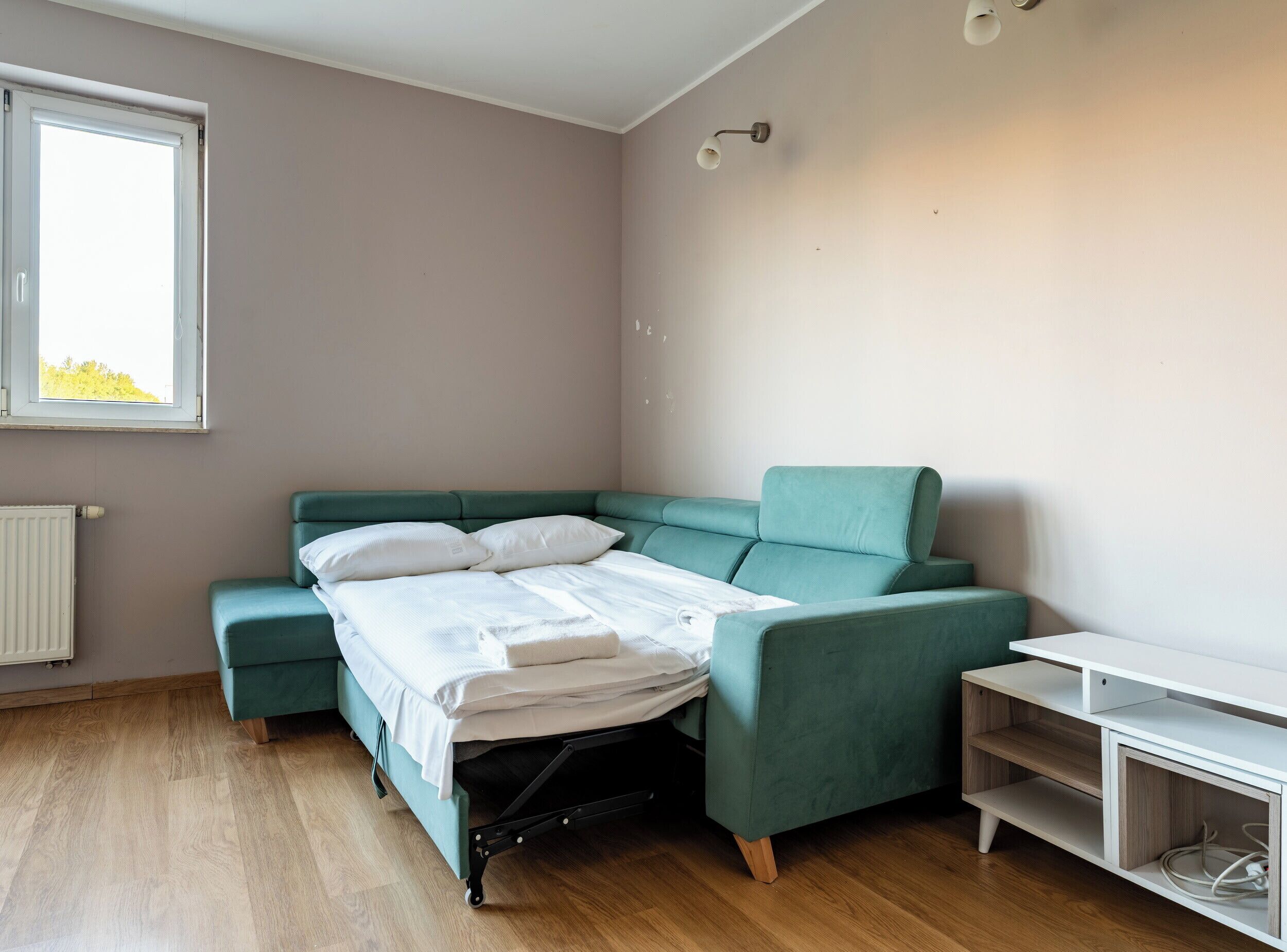 A room with a bed, a green sofa, a small table, and a window.