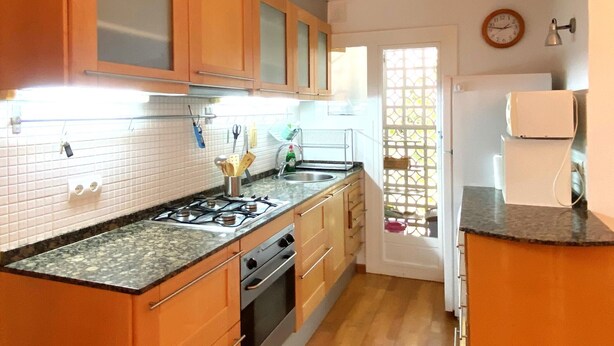 A kitchen with wooden cabinets, a gas stove, a sink, and a window with a decorative screen. - Apartment with a sea views in Levantina, Sitges (Sitges)