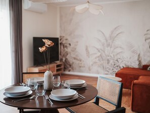A dining area with a round table set for four, a vase with dried flowers, and a television in the background. - Penthouse, 200m from the beach w/ parking (Cubelles)