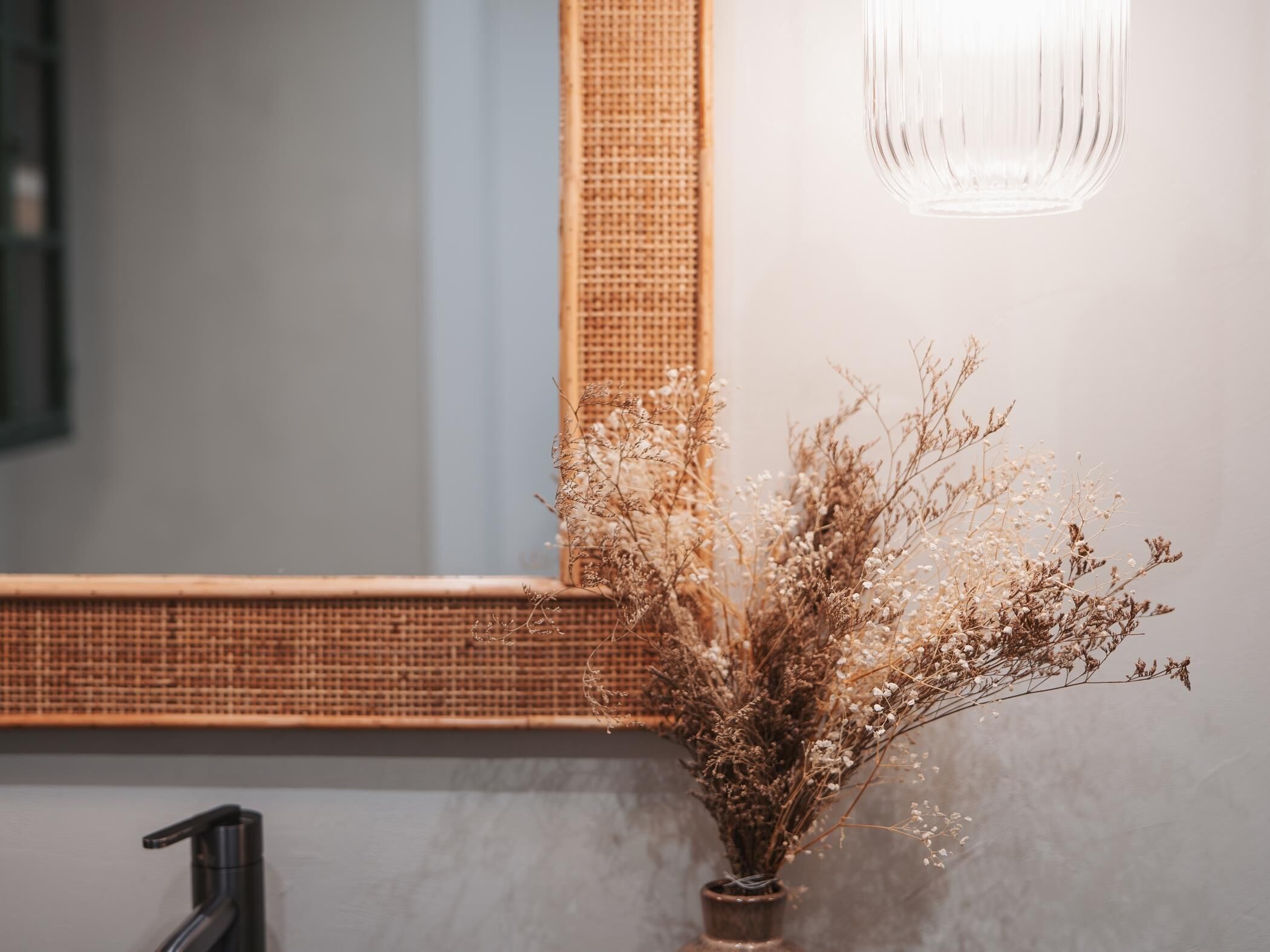 Une salle de bain avec un miroir, un vase contenant des fleurs séchées et un luminaire.
