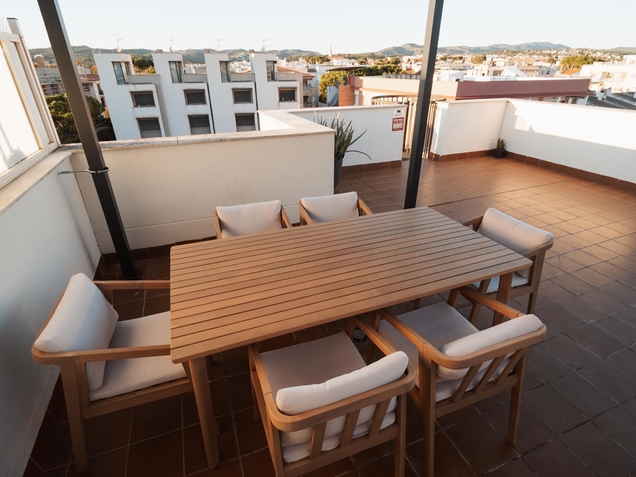 Eine Dachterrasse mit Holztisch und -stühlen, Blick auf die Stadtlandschaft und einem Blumentopf.