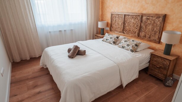 A hotel room with a large bed, a wooden headboard, two bedside lamps, a nightstand, and a decorative wall panel. - Penthouse, 200m from the beach w/ parking (Cubelles)