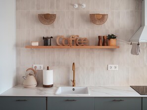 A kitchen with a marble countertop, a sink with a gold faucet, a kettle, a coffee-themed shelf, and a wall-mounted towel rack. - Penthouse, 200m from the beach w/ parking (Cubelles)