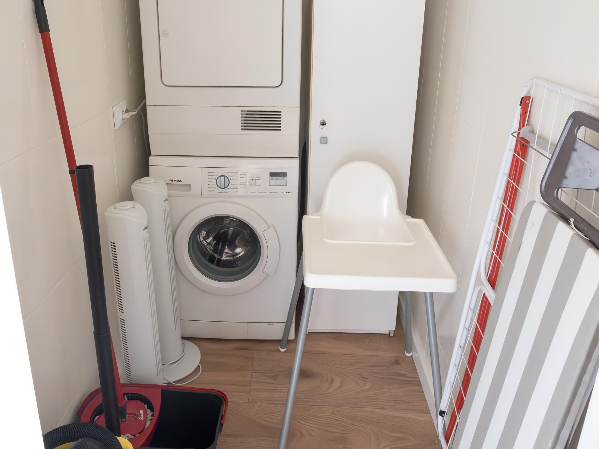 Een kleine wasruimte met een wasmachine, een droger en een klein krukje.