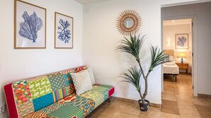 Ein Zimmer mit einem farbenfrohen Sofa, einem Blumentopf und gerahmten Bildern an der Wand.