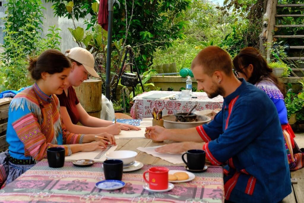 A group of people seated around a table with a tablecloth, plates, cups, and a teapot.