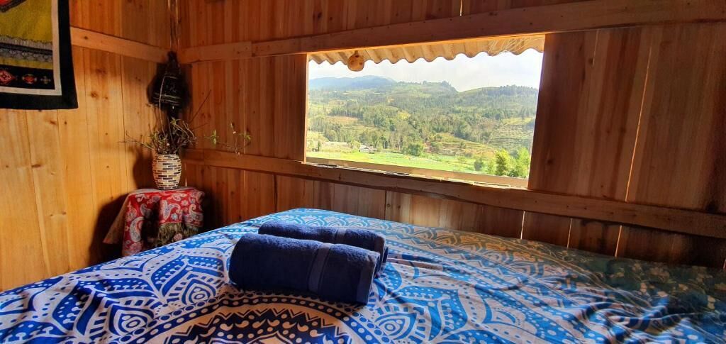 A wooden cabin room with a bed, a window, and a table with a vase.