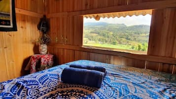 A wooden cabin room with a bed, a window, and a table with a vase.